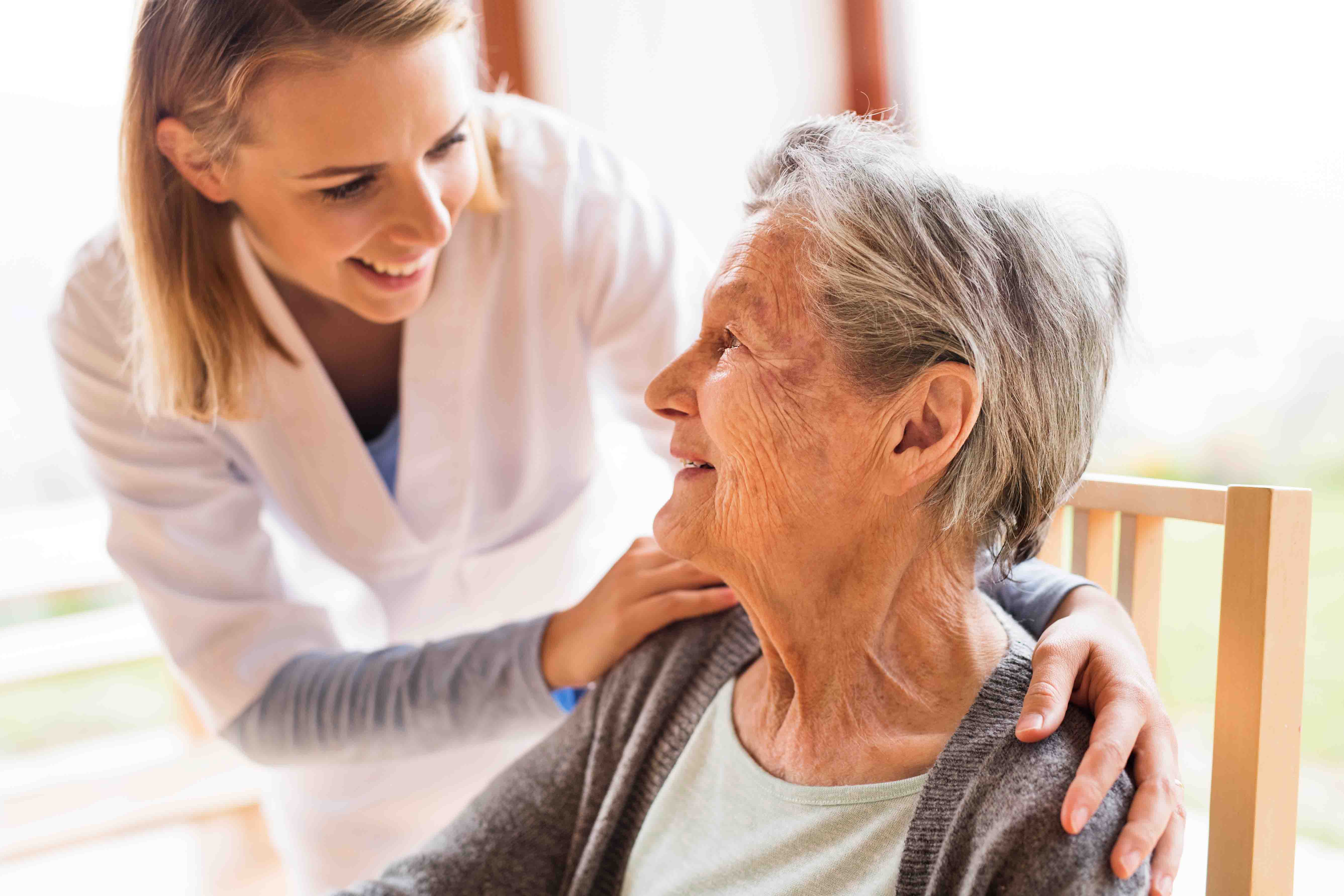 Kvinna på äldreboende och hennes sköterska tittar ömt på varandra och ler varmt